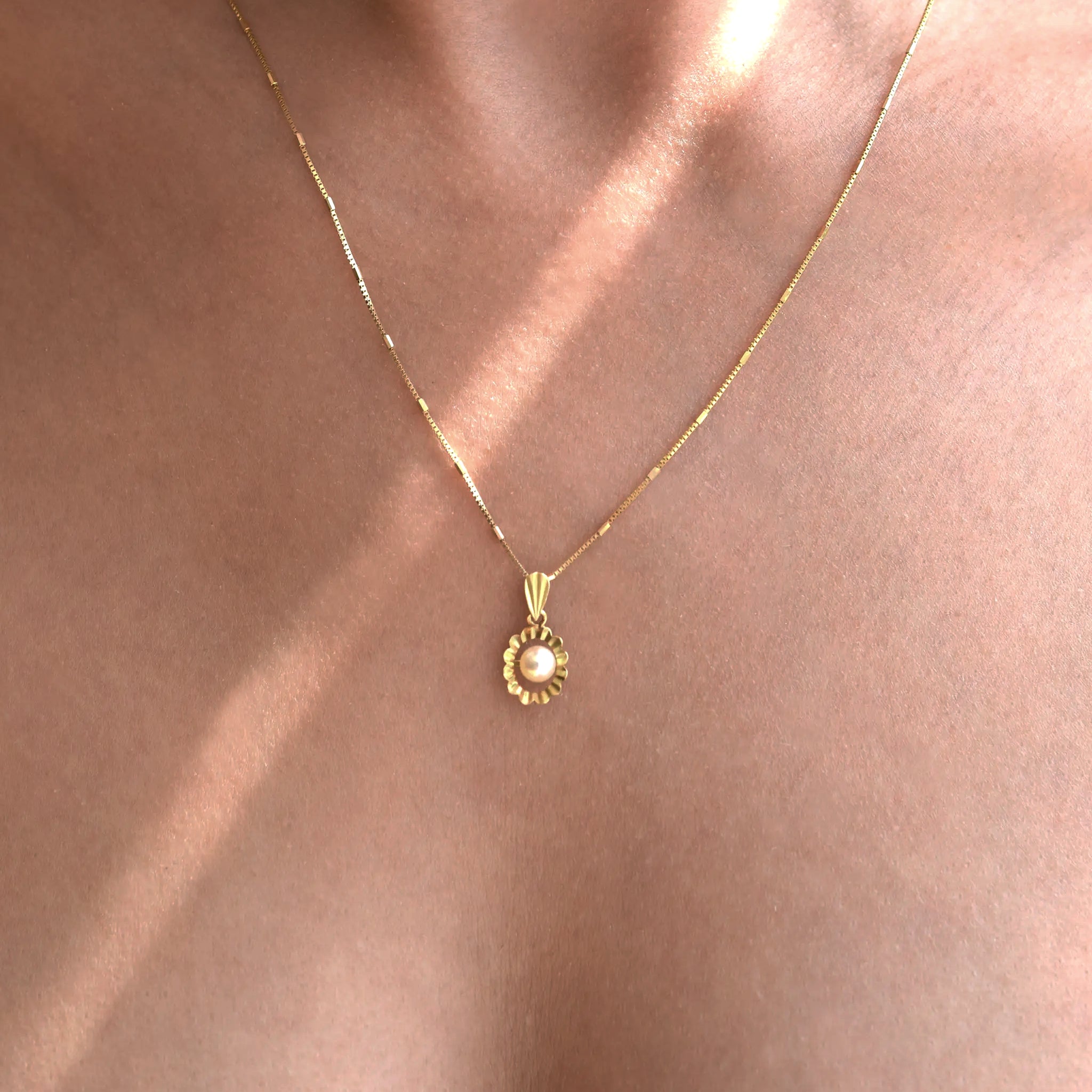 18 Karat Gold necklace with a pendant with a pearl on a person's neck.